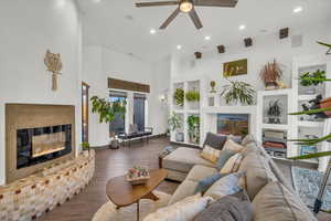 Living room with built in shelves, ceiling fan, a fireplace, and dark wood-type flooring