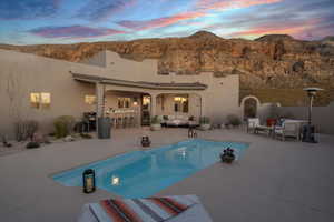 Pool at dusk featuring outdoor lounge area, a mountain view, exterior bar, area for grilling, and a patio