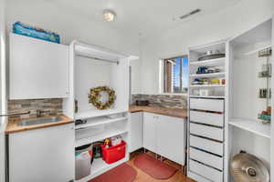 Interior space with wood counters, tasteful backsplash, sink, light hardwood / wood-style flooring, and white cabinetry