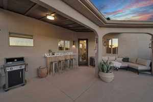 Patio terrace at dusk with grilling area, exterior bar, and an outdoor hangout area