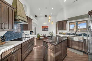 Kitchen featuring decorative backsplash, premium range hood, dark stone counters, black electric cooktop, and decorative light fixtures