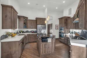 Kitchen with stainless steel appliances, decorative light fixtures, a center island with sink, a high ceiling, and dark hardwood / wood-style floors