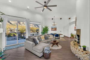 Living room with dark hardwood / wood-style floors, a towering ceiling, ceiling fan with notable chandelier, and a tiled fireplace