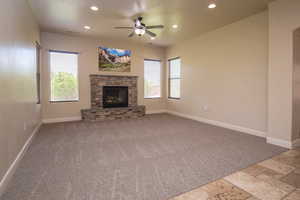 Unfurnished living room with ceiling fan and a stone fireplace