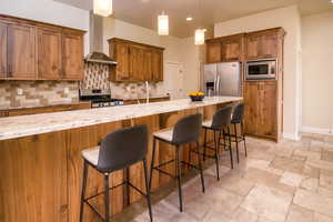 Kitchen with wall chimney exhaust hood, backsplash, pendant lighting, a breakfast bar area, and appliances with stainless steel finishes