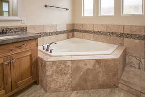 Bathroom with vanity, a relaxing tiled tub, and a healthy amount of sunlight