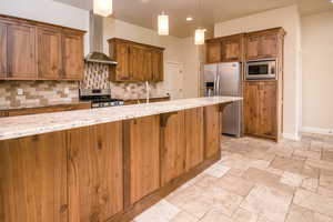 Kitchen featuring decorative light fixtures, light stone counters, wall chimney range hood, and appliances with stainless steel finishes