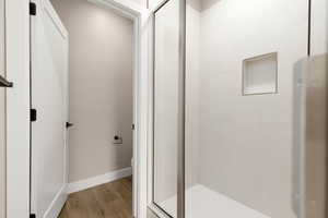 Bathroom with toilet, a shower with door, and hardwood / wood-style flooring