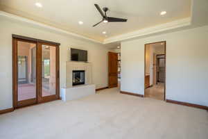 Unfurnished living room featuring a fireplace, light carpet, a tray ceiling, and ceiling fan