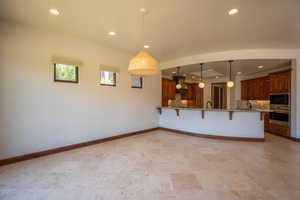 Kitchen with black microwave, hanging light fixtures, tasteful backsplash, oven, and a kitchen bar