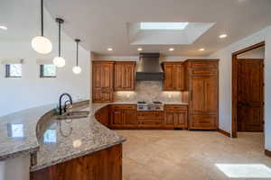 Kitchen featuring kitchen peninsula, light stone countertops, custom exhaust hood, sink, and decorative light fixtures