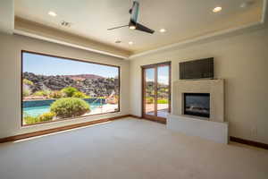 Unfurnished living room with a tray ceiling, a tiled fireplace, ceiling fan, and light carpet