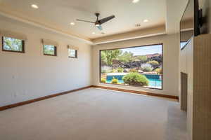 Empty room featuring a raised ceiling, ceiling fan, and light carpet