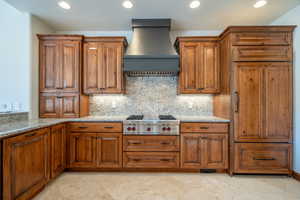 Kitchen with premium range hood, decorative backsplash, light stone countertops, and stainless steel gas cooktop