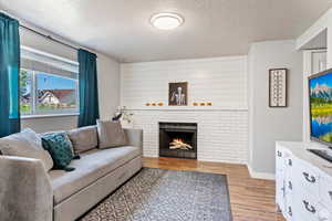 Living room featuring light hardwood / wood-style flooring, a textured ceiling, and a brick fireplace