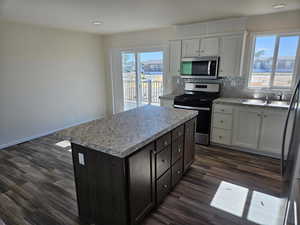 Kitchen featuring appliances with stainless steel finishes, dark hardwood / wood-style flooring, sink, a center island, and white cabinetry