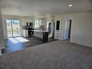 Kitchen with light stone countertops, white cabinetry, a center island, dark carpet, and appliances with stainless steel finishes