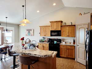 Kitchen with hanging light fixtures, a chandelier, vaulted ceiling, a center island with sink, and black appliances