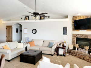 Living room with light carpet, vaulted ceiling, ceiling fan, and a stone fireplace