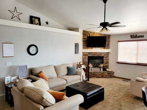 Living room featuring a stone fireplace, ceiling fan, carpet, and vaulted ceiling