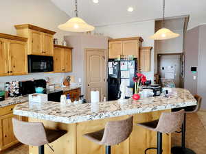 Kitchen with a kitchen bar, pendant lighting, a center island with sink, and black appliances