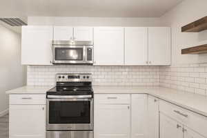 Kitchen with backsplash, white cabinetry, wood-type flooring, and appliances with stainless steel finishes