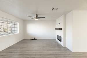 Unfurnished living room with ceiling fan, a large fireplace, and light wood-type flooring