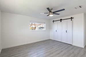 Unfurnished bedroom featuring a barn door, ceiling fan, a closet, and light wood-type flooring