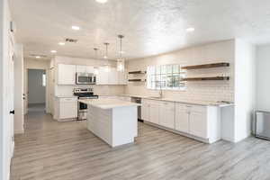 Kitchen featuring a center island, white cabinets, decorative light fixtures, and appliances with stainless steel finishes