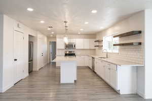 Kitchen featuring pendant lighting, a center island, white cabinets, sink, and appliances with stainless steel finishes