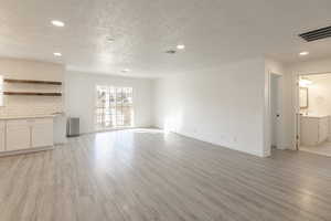 Unfurnished living room with sink, a textured ceiling, and light hardwood / wood-style flooring