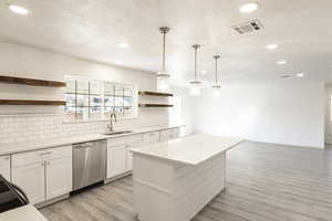 Kitchen featuring pendant lighting, a center island, white cabinets, sink, and stainless steel dishwasher