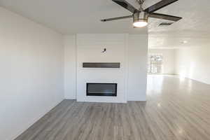 Unfurnished living room featuring ceiling fan, a large fireplace, a textured ceiling, and light hardwood / wood-style flooring