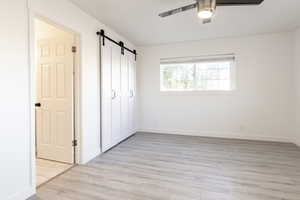 Unfurnished bedroom featuring ceiling fan, a barn door, a closet, and light hardwood / wood-style flooring