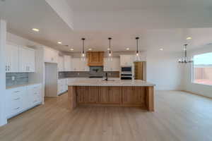 Kitchen with white cabinets, decorative light fixtures, stainless steel appliances, and a spacious island