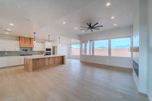 Kitchen with ceiling fan, built in microwave, pendant lighting, white cabinetry, and an island with sink