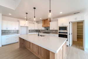 Kitchen featuring a large island with sink, stainless steel appliances, white cabinetry, and sink