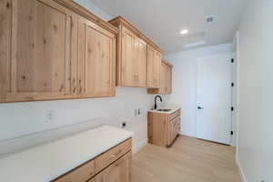 Laundry room featuring cabinets, sink, light hardwood / wood-style flooring, washer hookup, and hookup for an electric dryer