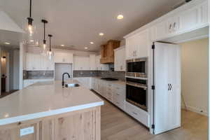 Kitchen with pendant lighting, a spacious island, sink, white cabinetry, and stainless steel appliances