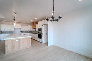 Kitchen with appliances with stainless steel finishes, sink, a center island with sink, white cabinets, and hanging light fixtures