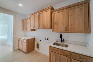 Washroom with sink, cabinets, hookup for an electric dryer, light hardwood / wood-style flooring, and hookup for a washing machine