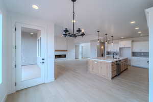 Kitchen featuring white cabinetry, dishwasher, backsplash, a large island with sink, and decorative light fixtures