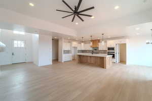 Kitchen featuring pendant lighting, a large island with sink, white cabinets, ceiling fan with notable chandelier, and appliances with stainless steel finishes