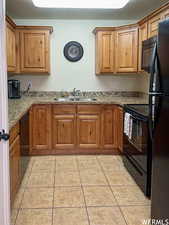 Kitchen featuring light stone countertops, sink, light tile patterned floors, and black appliances