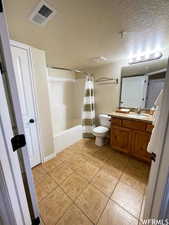 Full bathroom featuring shower / tub combo, tile patterned floors, vanity, a textured ceiling, and toilet