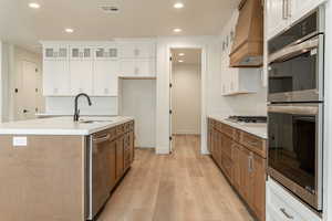 Kitchen featuring white cabinets, custom range hood, sink, and a kitchen island with sink