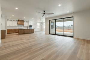 Unfurnished living room featuring light wood-type flooring, a textured ceiling, ceiling fan with notable chandelier, and sink