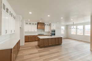 Kitchen with a center island with sink, sink, gas stovetop, custom range hood, and white cabinetry