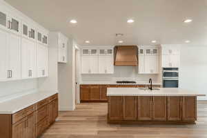 Kitchen featuring custom exhaust hood, a kitchen island with sink, white cabinets, sink, and appliances with stainless steel finishes