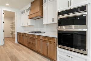 Kitchen with custom exhaust hood, white cabinetry, stainless steel appliances, and light hardwood / wood-style flooring